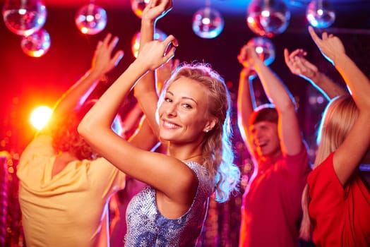 Joyful girl dancing in night club with her friends on background