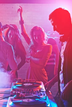 Dancing girls enjoying party by turntables of deejay adjusting sound