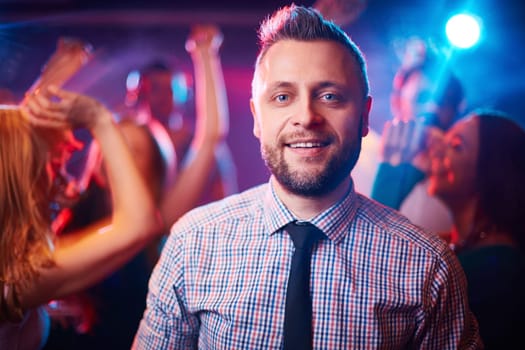 Handsome man looking at camera at disco among his dancing friends