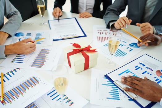 Group of employees analyzing marketing data on Christmas eve at workplace with champagne and giftbox
