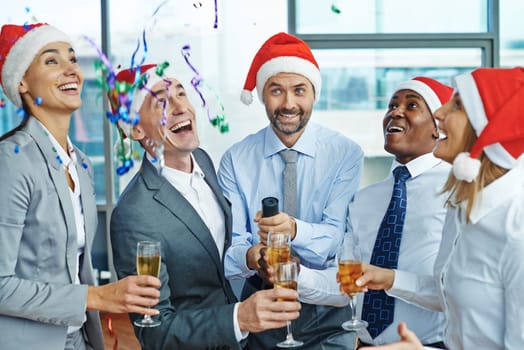 Happy colleagues in Santa caps with champagne having Christmas fun in office