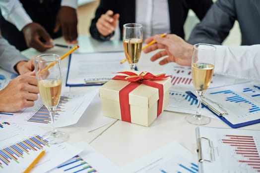 Hands of colleagues discussing papers on Christmas eve at workplace with champagne and giftbox