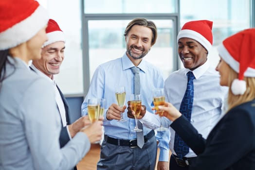 Successful colleagues in Santa caps toasting with champagne at corporate party