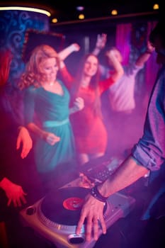 Hand of deejay on turntable and group of dancing girls on background