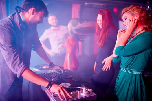 Glamorous girls dancing by dj adjusting sound on turntables in night club