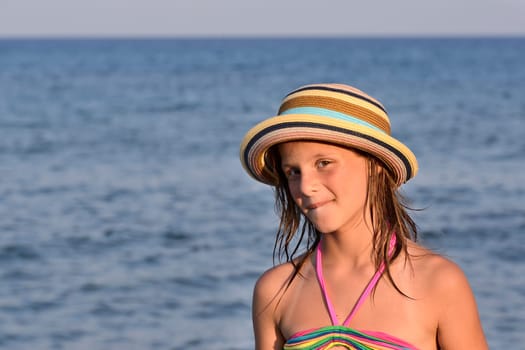 Little girl on the beach at sunset, portrait smiling with a large hat.