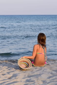 Little girl on the beach at sunset, portrait smiling with a large hat.