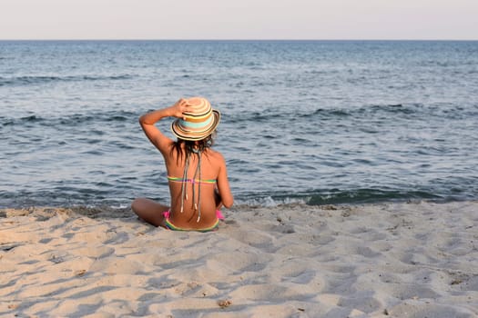 Little girl on the beach at sunset, portrait smiling with a large hat.