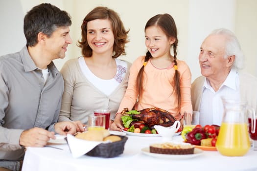 Happy family at Thanksgiving table going to eat roasted turkey held by cute girl