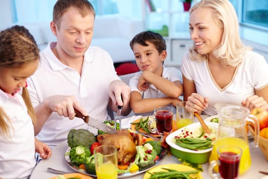 Happy young family sitting by festive table and eating traditional Thanksgiving food