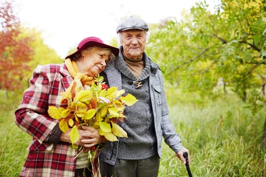 Happy senior woman with autumn leaves leaning to her husband in park