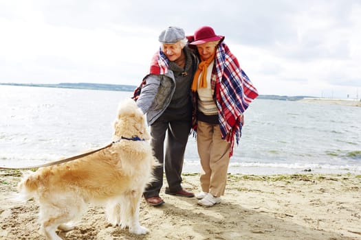 Retired couple playing with dog by seaside on autumn weekend