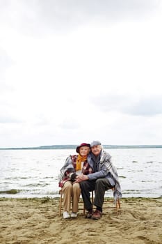 Retired seniors sitting by seaside and looking at camera
