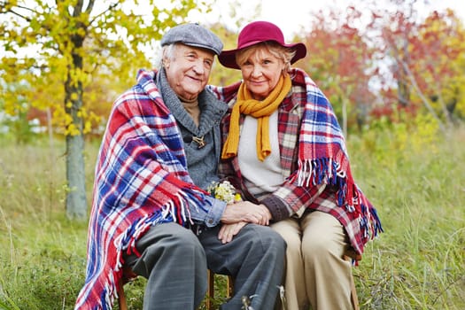 Retired man and woman in warm clothes resting outdoors in autumn