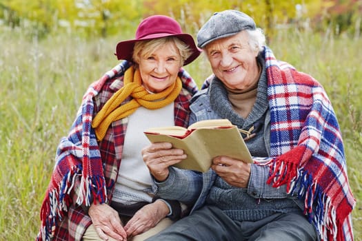 Retired seniors reading book outdoors
