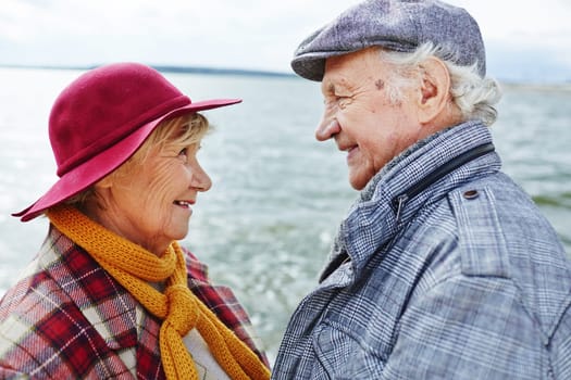 Retired couple in warm clothes looking at one another by seaside