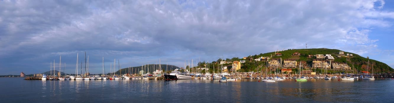 Summer coast panorama with boats in pier and cloudy skyline hill view of Piriapolis, Uruguay from the sea.