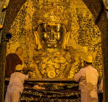 Early morning senior monk applying gold leaf to Mahamuni Buddha in Mandalay, Myanmar