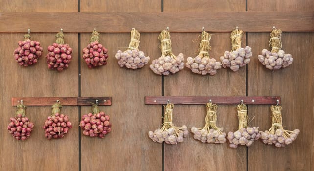 String of red onion and garlic bulbs hanging on wooden wall