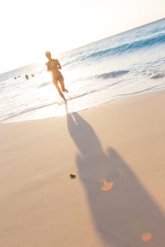 Happy woman enjoying in summer, running joyfully on tropical beach in sunset. Beautiful caucasian model wearing bikini on vacations on sandy beach. Footprints in sand.