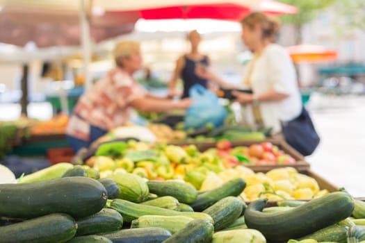Farmers&#39  food market stall with variety of organic vegetable. Vendor serving and chating with customers.