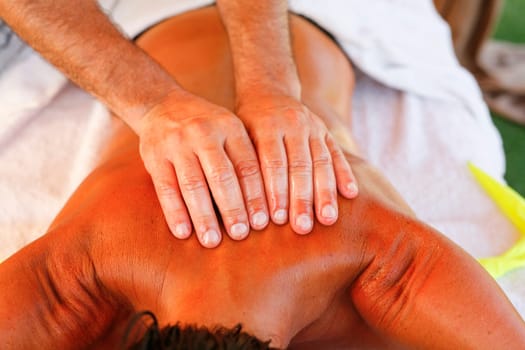 Massage therapist working with suntanned beautiful woman at  beach resort