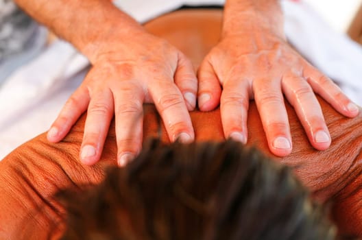 Massage therapist working with suntanned beautiful woman at  beach resort