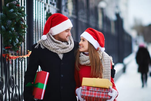 Amorous Santas with giftboxes looking at one another outdoors