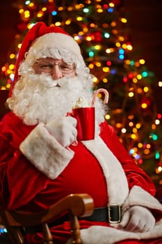Santa Claus with cup of latte on background of Christmas tree
