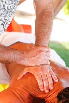 Massage therapist working with suntanned beautiful woman at  beach resort