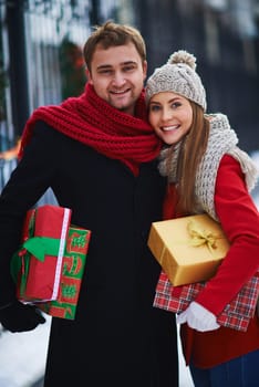 Amorous couple with giftboxes looking at camera outdoors