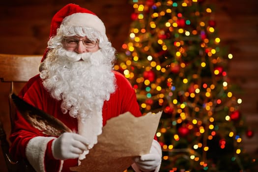 Senior man in costume of Santa Claus holding feather and Christmas letter