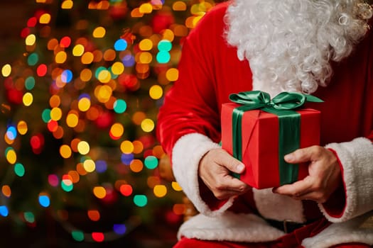 Red giftbox bound by silk green ribbon held by Santa