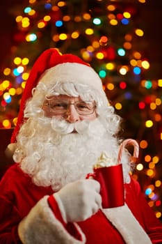 Santa Claus relaxing and having latte on background of Christmas tree