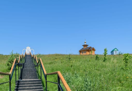 Metal stairs with railings leading up to the place of prayer and a wooden chapel near the small house on the hill.