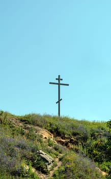 Big old wooden Orthodox cross on a hill on a clear blue cloudless sky on a summer day