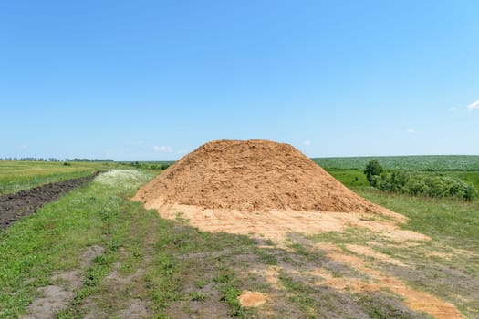 Big pile of yellow sand in the middle of the field with sprouted crop yields under a blue cloudy sky on a summer day