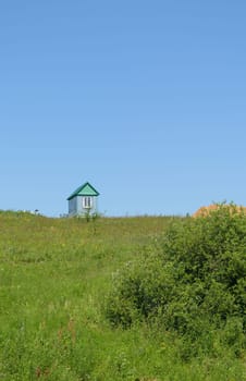 A lone house stands on a green grass hill.