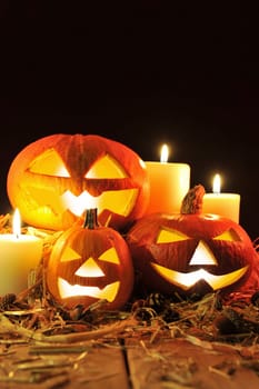 Three illuminated Halloween pumpkins with straw on old weathered wooden boards against a red-brown background in red light