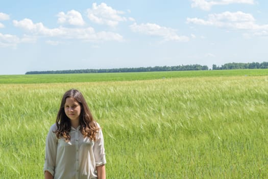 Young seventeen year old girl standing on a background of green field on a summer day.