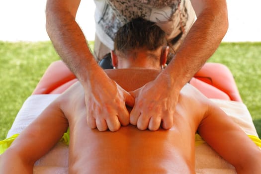 Massage therapist working with suntanned beautiful woman at beach resort