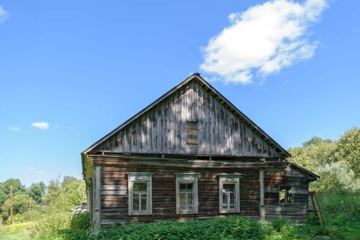 Old dilapidated abandoned wooden house on forest clearing. Blue sky with clouds on sunny clear day