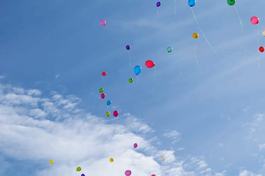 Many colored balloons fly (hover) in the blue sky with clouds