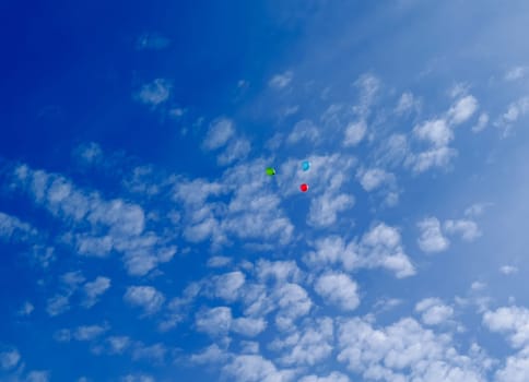 Three multi-colored balloons fly (hover) in the blue sky with clouds