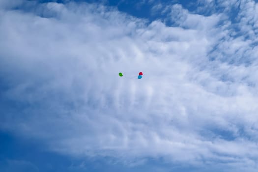 Three multi-colored balloons fly (hover) in the blue sky with clouds