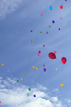 Many colored balloons fly (hover) in the blue sky with clouds