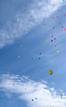 Many colored balloons fly (hover) in the blue sky with clouds