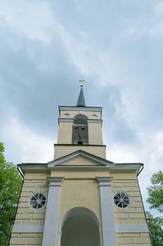 Bell tower of the chapel in the countryside in the background of the cloudy sky.