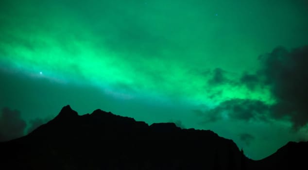The Northern Lights emerge through the clouds in remote Alaska