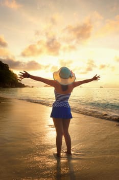 Tourist girl in a swimsuit blue and white striped hat standing on beach with pleasure the beautiful landscape of sky and sea during sunrise, Miang island, Similan National Park, Phang Nga, Thailand